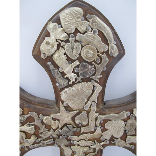 Traditional Mexican folk art wall cross made from carved wood and heavily embellished with metal Milagro charms. Larger...