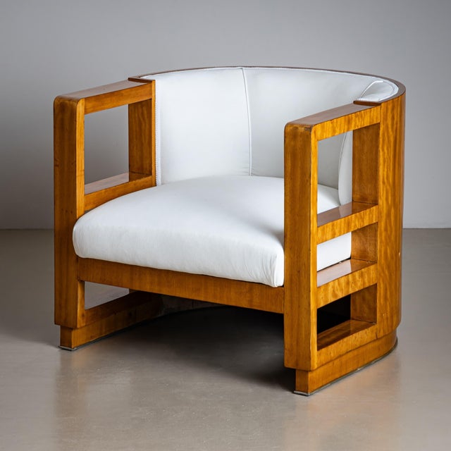 An elegant Art Deco armchair featuring a softly rounded frame and distinctive rectangular cut-outs at armrest height....