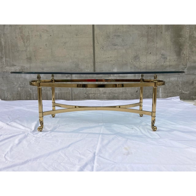 Vintage French hollywood regency style brushed brass base, 5/8” thick rounded edge elliptical glass top coffee table,...