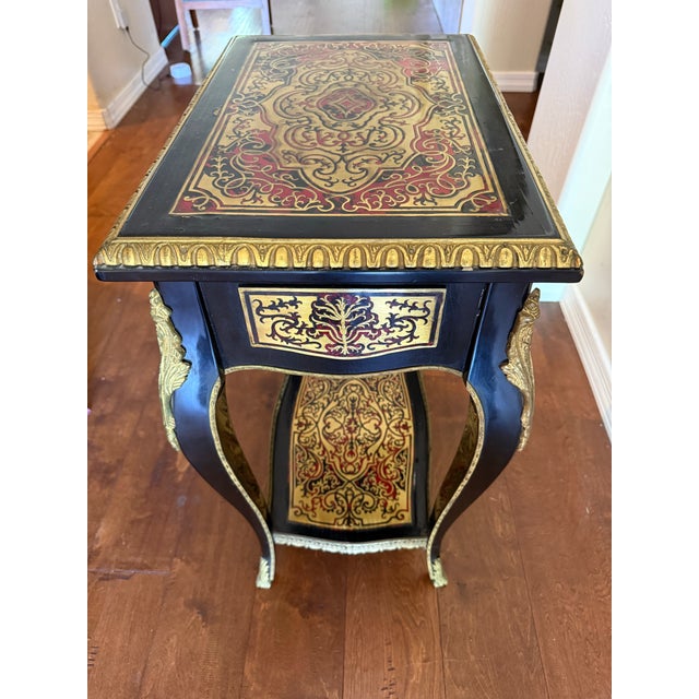 Elegant vintage French-style side table featuring a black lacquered finish with ornate red and gold scrolling decoration...