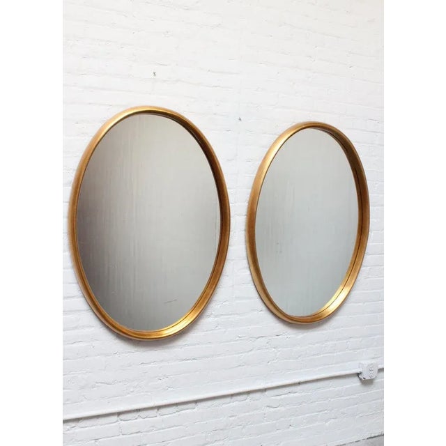 Pair of wide, oval-form Labarge mirrors composed of inset glass within deep, gold leaf frames. There is minor wear to the...
