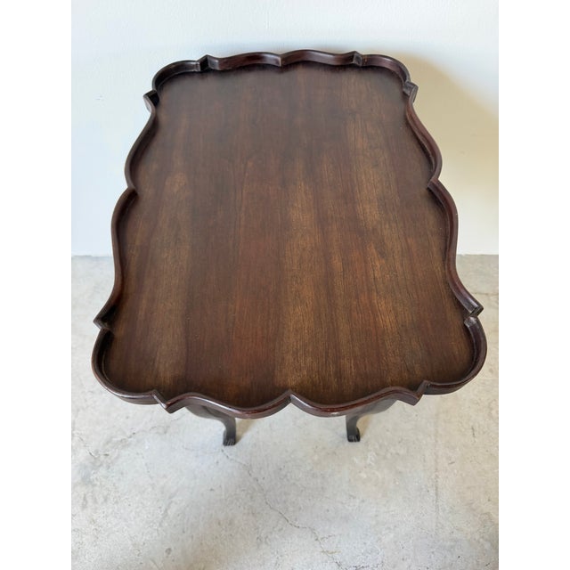 Elegant antique French-style side table crafted in rich mahogany, featuring a distinctive serpentine scalloped gallery top...