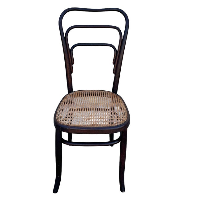 Early Modernist Thonet number 144 side chair features an elegant, sculptural frame crafted from warm-toned bentwood with...