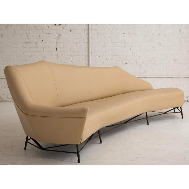 A mid century French attributed sofa. Angular gothic silhouette. Iron base frame. Cream vinyl upholstery with brass brad...
