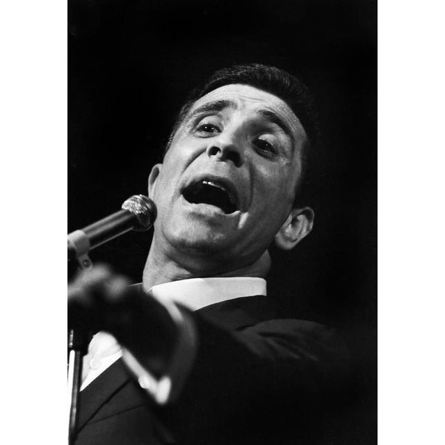 This photo shows the French singer Gilbert Bécaud during a concert in East Berlin in 1964. In the image, Bécaud is...