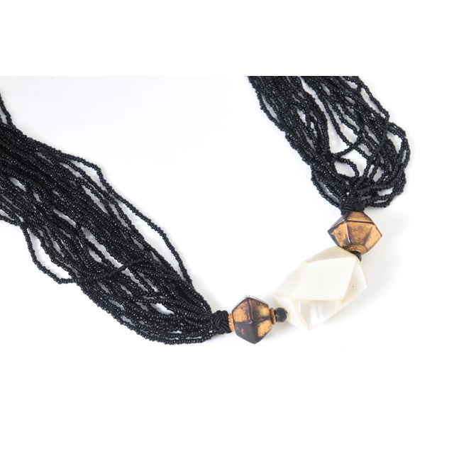 Vintage 18-strand black glass bead necklace featuring a large geometric bead with mother-of-pearl sections between two...