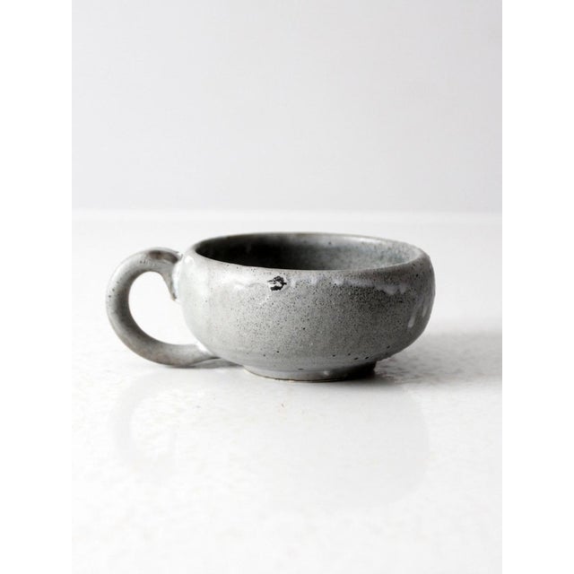 This vintage handmade studio pottery mug features a low, wide profile that gives it a distinctive look. The pale gray...