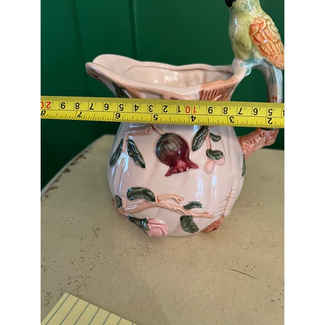 Majolica style pitcher with flowers and vines embossed on the pitcher. The handle is made of a parrot or cockatiel.