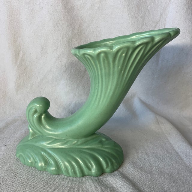 This item is a vintage mid-20th-century pastel green cornucopia (horn of plenty) art pottery vase, featuring a flared,...