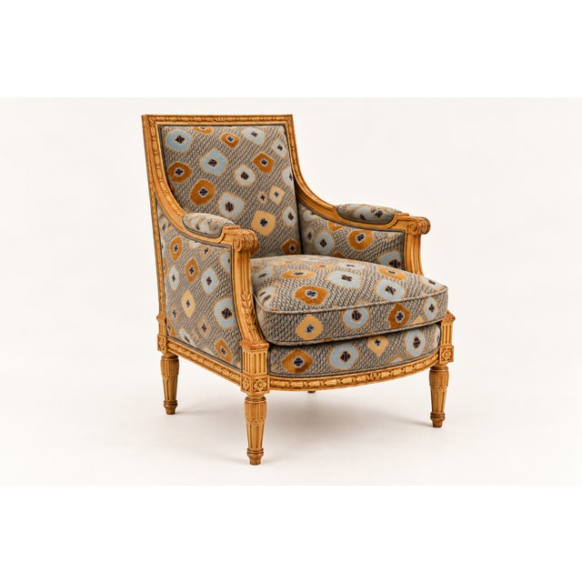 A sculptural armchair featuring a richly carved wood frame and geometric patterned upholstery in muted blue and ochre...