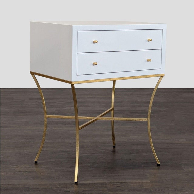 The nightstand features a sleek white lacquered finish, two spacious drawers with gold knobs, and a sturdy gold metal...