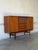 This substantial sideboard features a broad profile with smooth sliding doors. The center reveals three drawers beneath a...