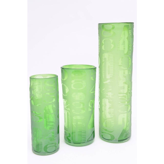 In these vintage 1980's set of 3 graduated green glass vases hint at an abstract design of etched letters and numbers. The...