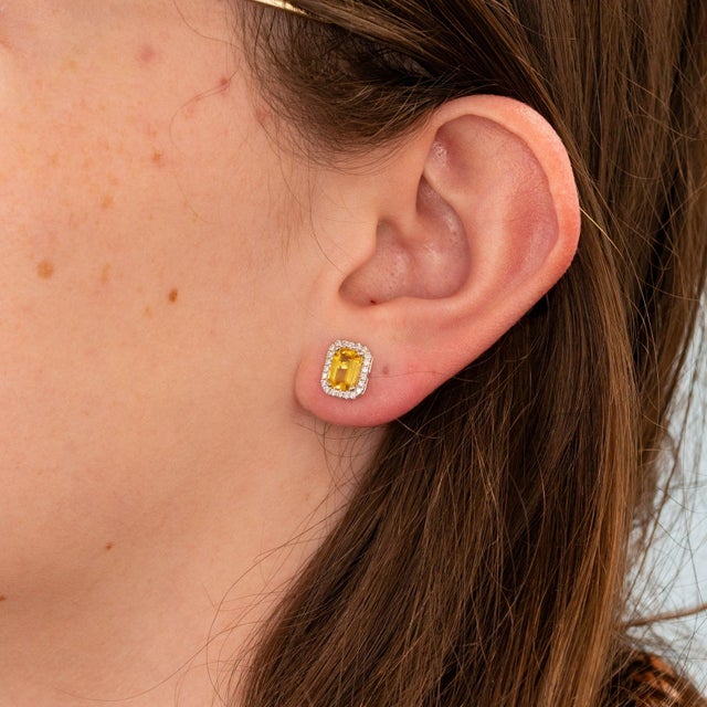Sunlit yellow sapphires rest within a sparkling halo of diamonds in these emerald-cut stud earrings, crafted in solid 14K...
