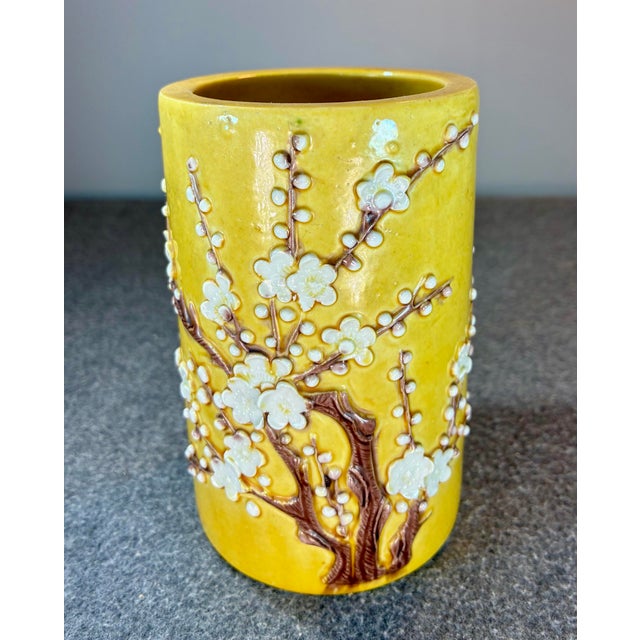 Yellow glazed brushpot with applied decoration of a blossoming plum tree in tones of brown and white.