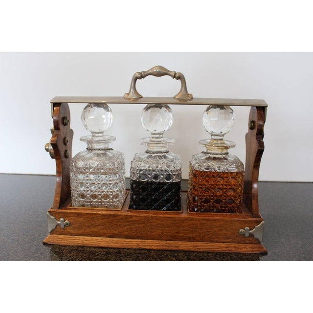 Antique English oak tantalus dating to the late 1800s, featuring a beautifully crafted wooden frame fitted with three...