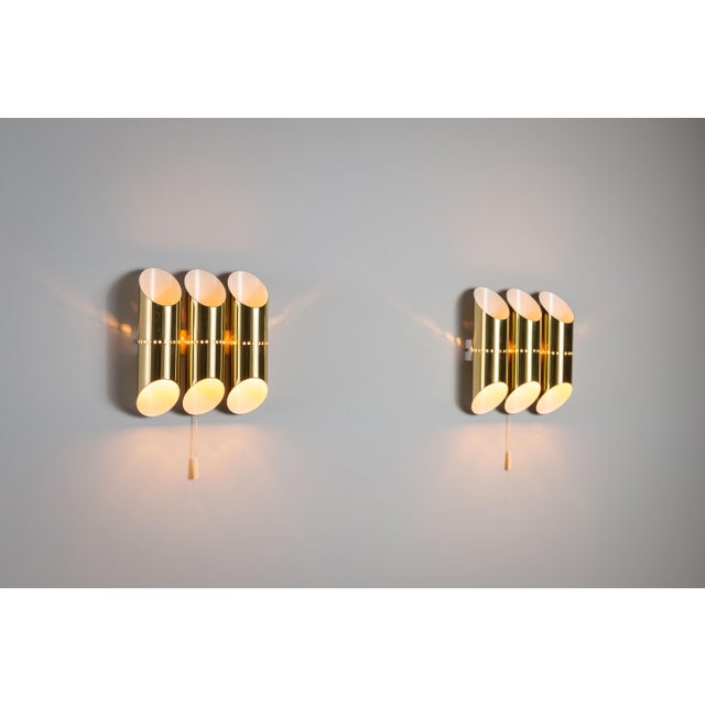 This pair of vintage wall lamps features an elegant brass design with a distinctive triple-cylindrical shade. Each...