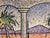 This mixed media artwork features a vibrant scene that juxtaposes a fish bowl with a tropical landscape, where palm trees...