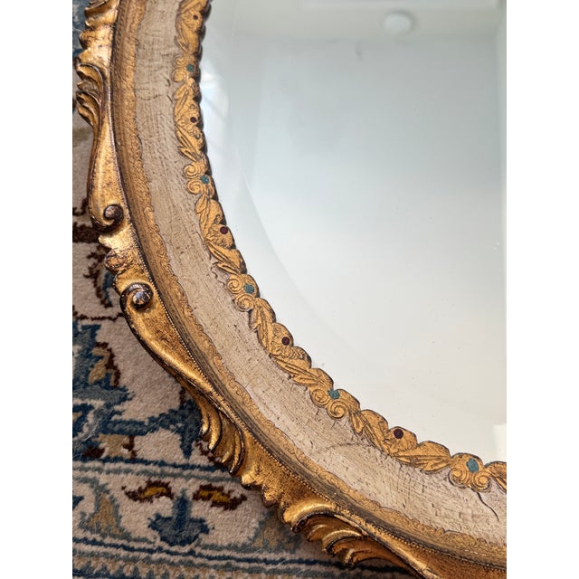Listing is for a Italian vintage wooden oval mirror painted cream with gilt scrollwork borders accented with pops of deep...