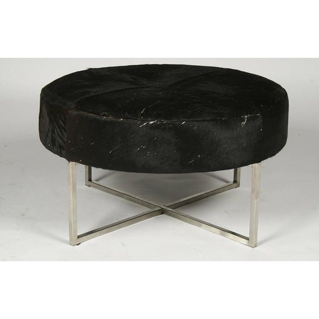 A Mid-Century Modern cow hide upholstered round bench or ottoman raised on a metal X-form base.