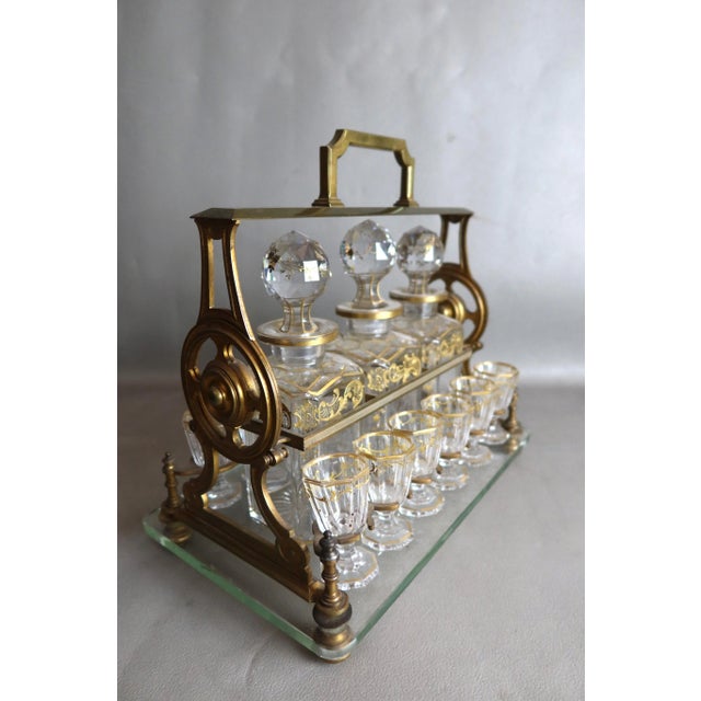 Liqueur cabinet with bronze and gilded brass mounts on a glass top. This cabinet contains three bottles and twelve gilded...
