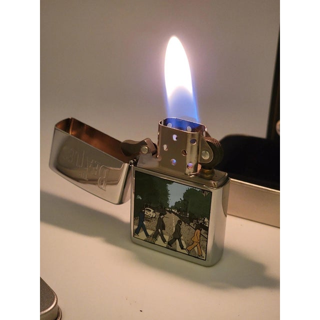 This rare Zippo lighter features a design inspired by The Beatles' iconic album "Abbey Road" from 1996. It is a retired...
