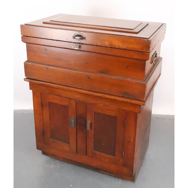 Antique tool cabinet made of pine with two sections and swivels on casters. The recessed upper tier features a hinged...