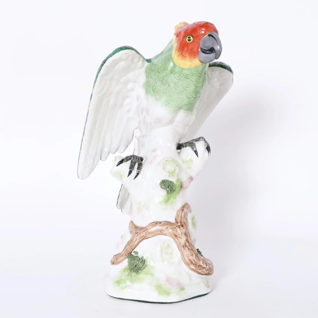 Charming life size porcelain parrot hand decorated in vivid tropical colors, glazed and perched on a tree trunk. Signed...