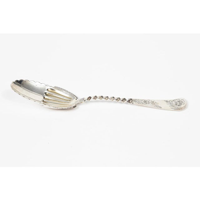 Ornate sterling silver serving spoon featuring an engraved floral handle that is twisted where it meats the bowl.. The...