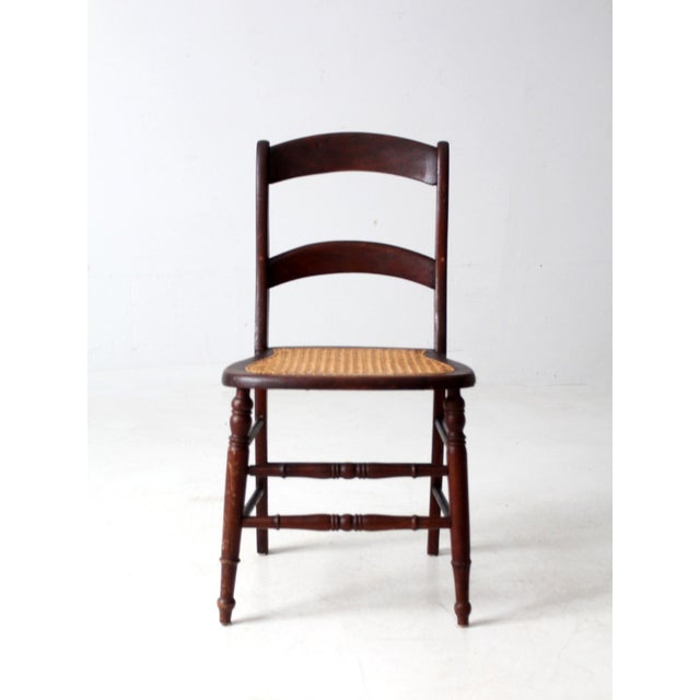A late 19th to early 20th century American ladder-back chair with gently arched double slats and a woven cane seat. The...