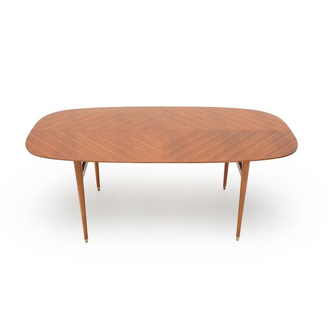 Elegant 1950s dining table featuring a refined veneered top with a diagonal herringbone pattern, creating a balanced and...