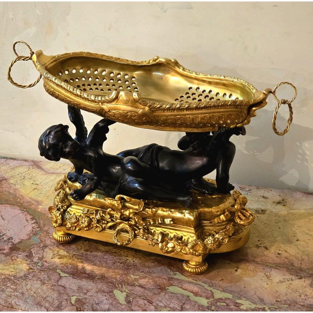 Exquisite French Rococo-style centerpiece bowl featuring elegant cherub figures in a rich bronze finish supporting an...