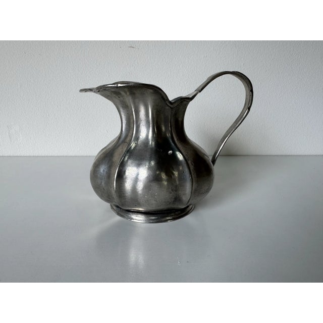 A charming vintage Italian pewter small pitcher featuring a scalloped rim and bulbous body with elegant curves. The handle...