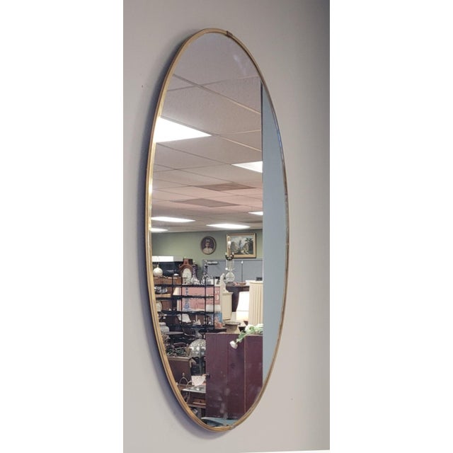 Find mid-century modern large oval mirror with thin brass laminated frame and wood backing. Measuring 41 in tall by 29 in...
