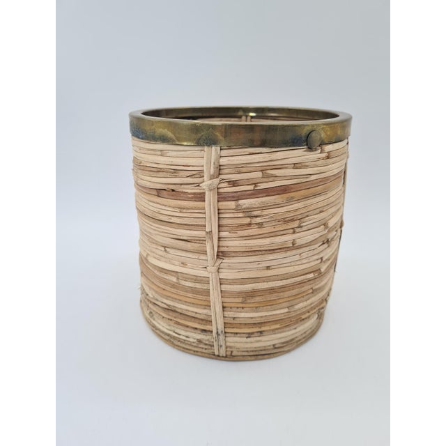 A stylish container made of natural rattan with a brass rim, designed in the aesthetic of 1960s–70s Italian design. The...