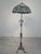 Tiffany-Style Metalwork Floor Lamp Tiffany-style floor lamp with a metal base and a colorful floral shade. Tall, stable...