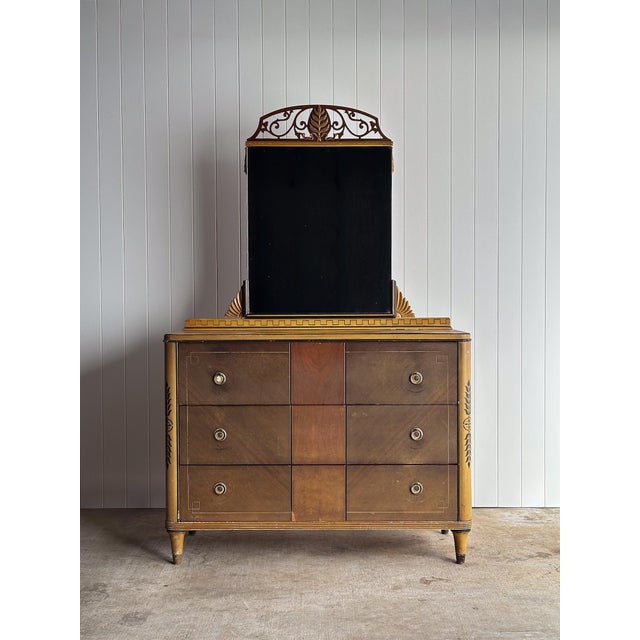 A richly detailed neoclassical chest of drawers with integrated mirror back, finished in warm layered paint and time-...