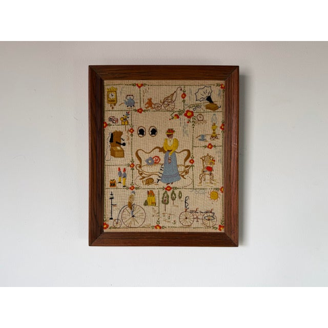 A charming vintage framed needlepoint textile featuring a delightful whimsical domestic scene filled with nostalgic...