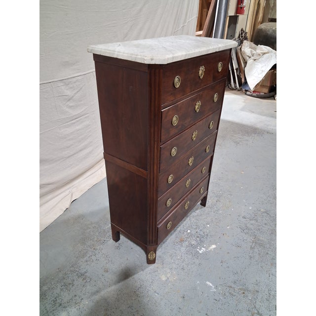 A French walnut semainier chest of drawers featuring a molded white marble top above six graduated drawers fitted with...