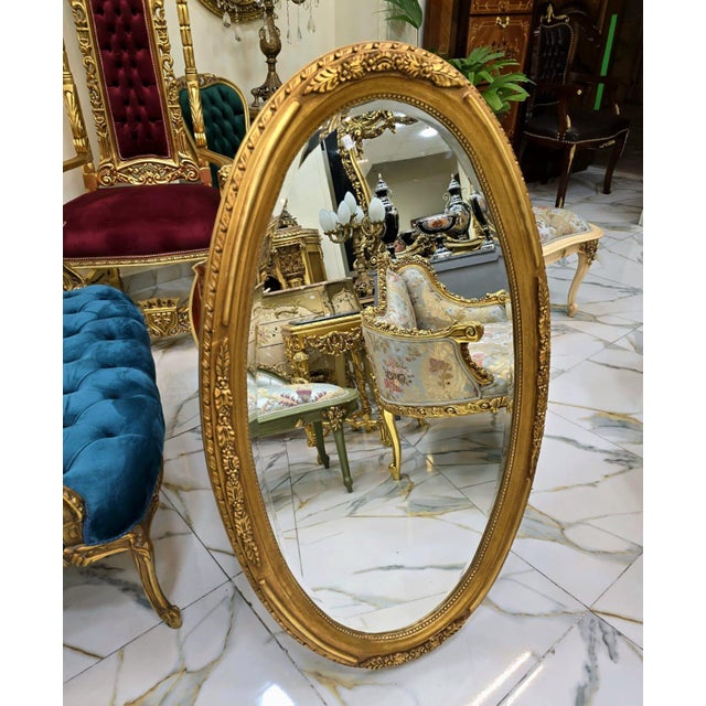Elegant Italian style vertical oval wall mirror featuring an ornate gold leaf frame beautifully enhanced with decorative...