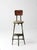 An early 20th century industrial drafting chair with a painted steel frame, solid wood seat and back, and an integrated...