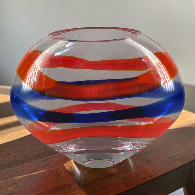 This stunning Italian hand-blown art glass vase features a unique oval shape with vibrant red and blue horizontal bands....