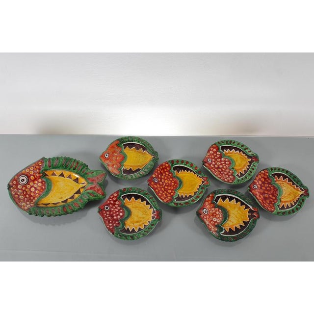A charming and charming set of six plates, including a large fish-shaped serving platter, in hand-decorated and glazed...