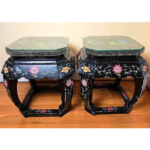 A pair of black lacquered hexagonal stools painted with flowers, with a Greek key border, sturdy curved legs and glass top...