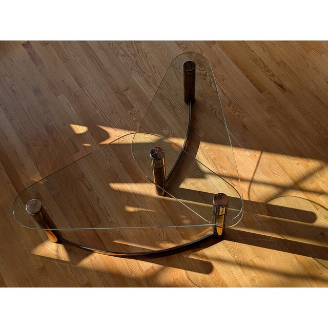 This vintage two-tier coffee table boasts a sculptural triangular form with a curved brass base and two kidney-shaped...