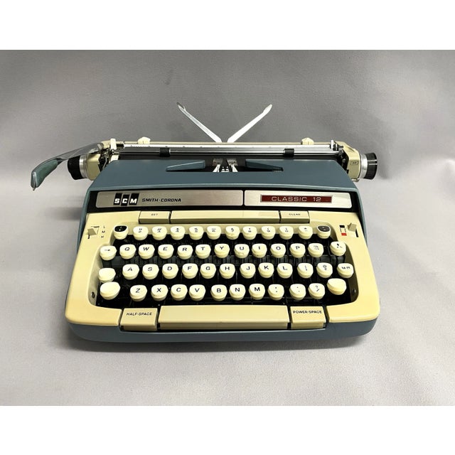 A mid-century Smith Corona Classic 12 typewriter. The portable typewriter is a stylish teal blue with a buff top and keys....