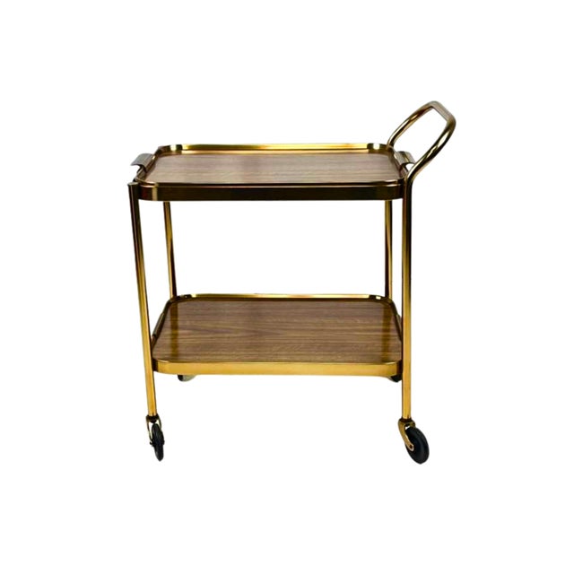Two-tier drinks trolley with detachable serving top tray. Ribbed gilt/brass metal frame, faux teak-form laminate shelves,...