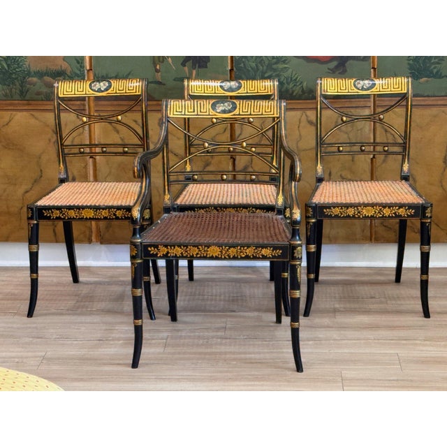 A set of four English Regency period black lacquer dining chairs with gilt decoration throughout consisting of three side...