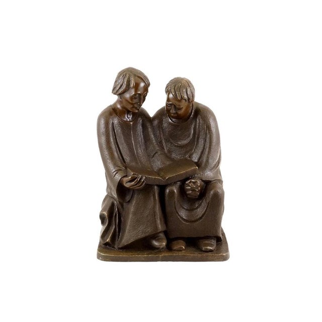 This bronze sculpture features two robed figures leaning toward one another in a moment of shared reading. The characters...
