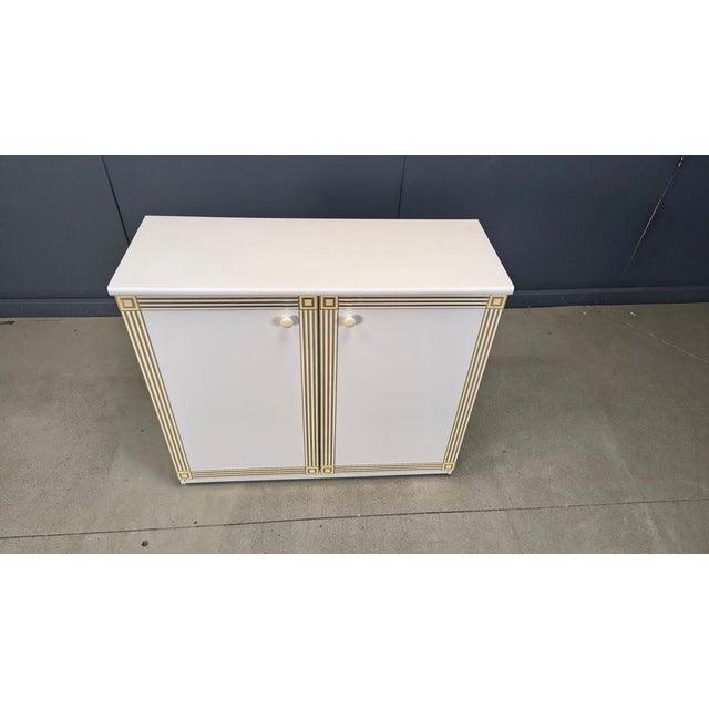 White lacquered wooden cabinet in holliwood regency style with inlaid brass. Handy cabinet with plenty of storage space....